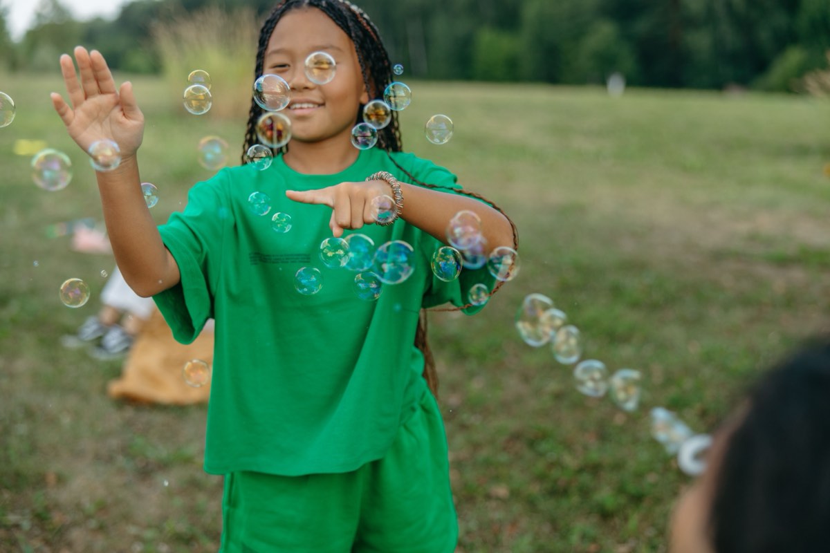 A camper laughing and reaching for soap bubbles in a field