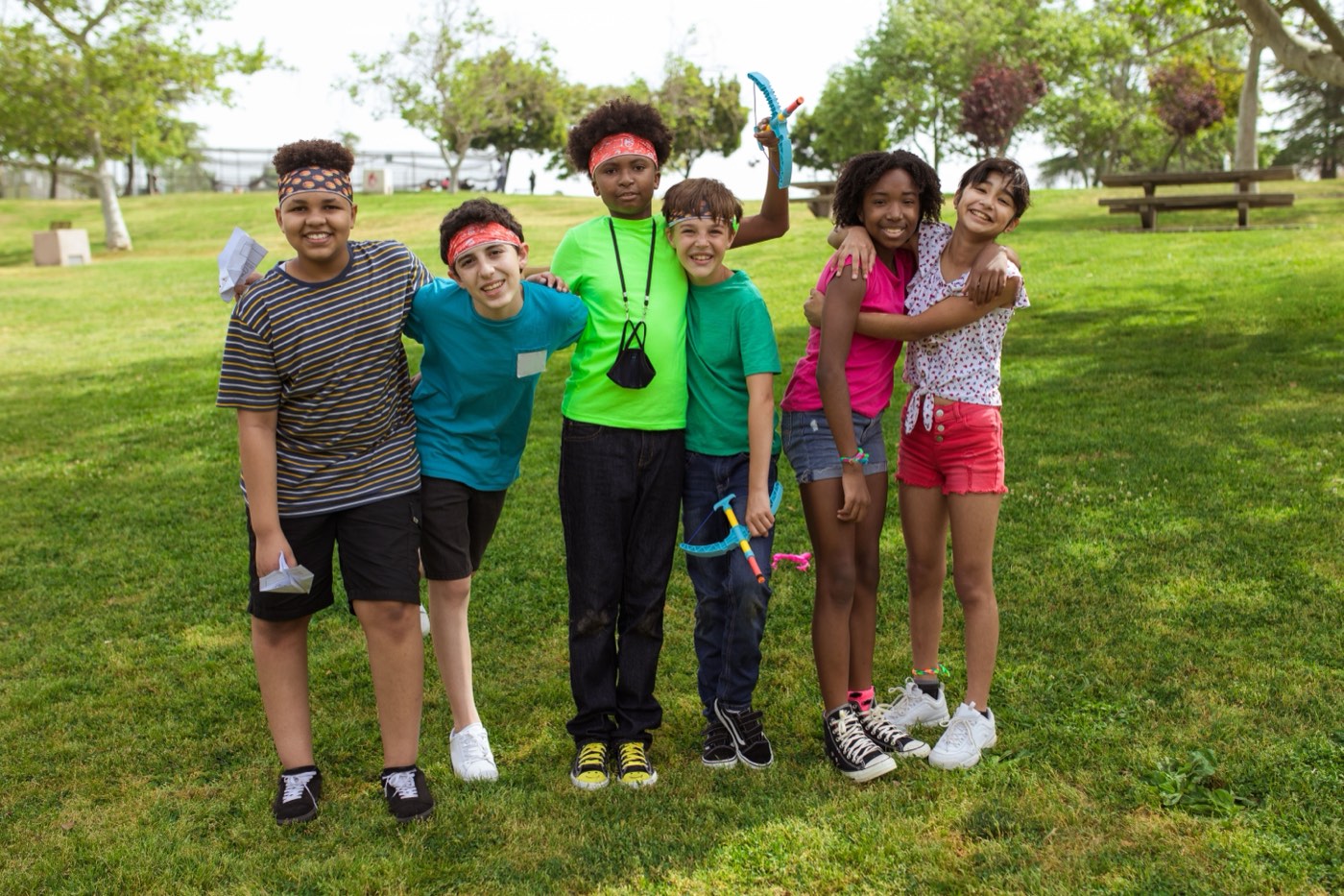A group of campers aged roughly eight to thirteen standing arm in arm on the grass, laughing