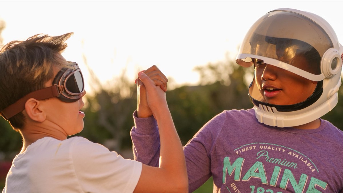 Two campers in flight goggles and a toy space helmet clasping hands in celebration