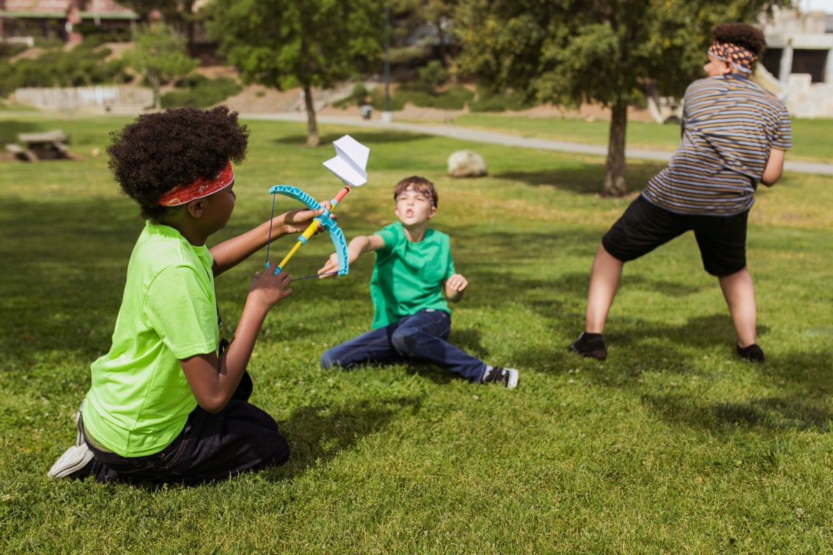 Campers on a lawn throwing and testing paper aeroplanes they have folded